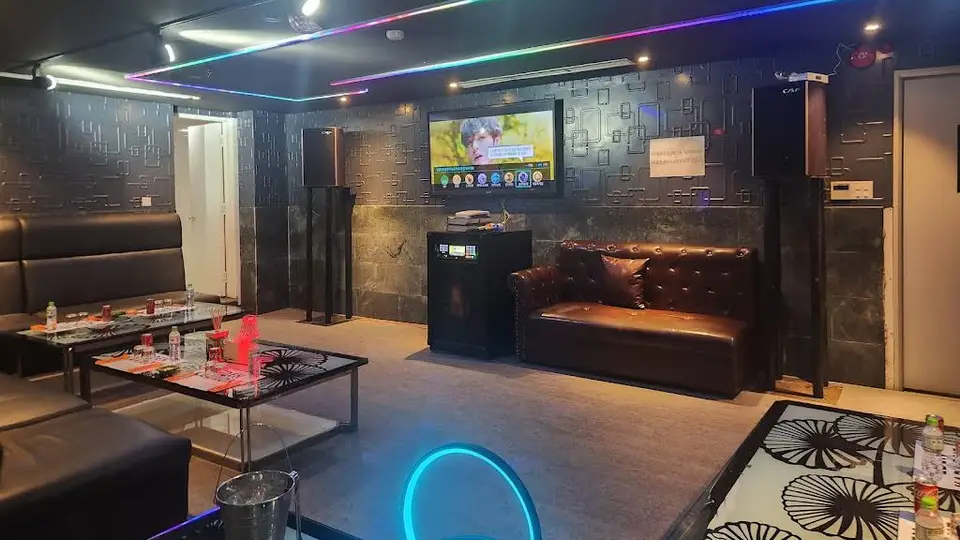 에덴 가라오케의 블랙 텍스처 벽면과 RGB 네온 천장 조명, 가죽 소파 및 대형 TV가 갖춰진 프라이빗 룸 내부
