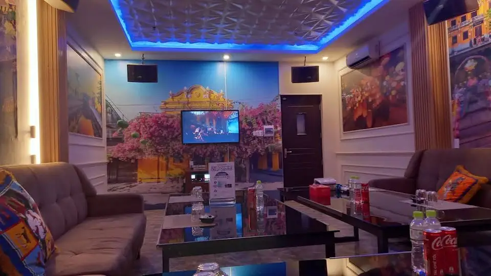 파란 LED 무드 조명과 호이안 벽화, 고급 소파와 글라스 테이블이 완비된 프라이빗 가라오케 룸 내부
