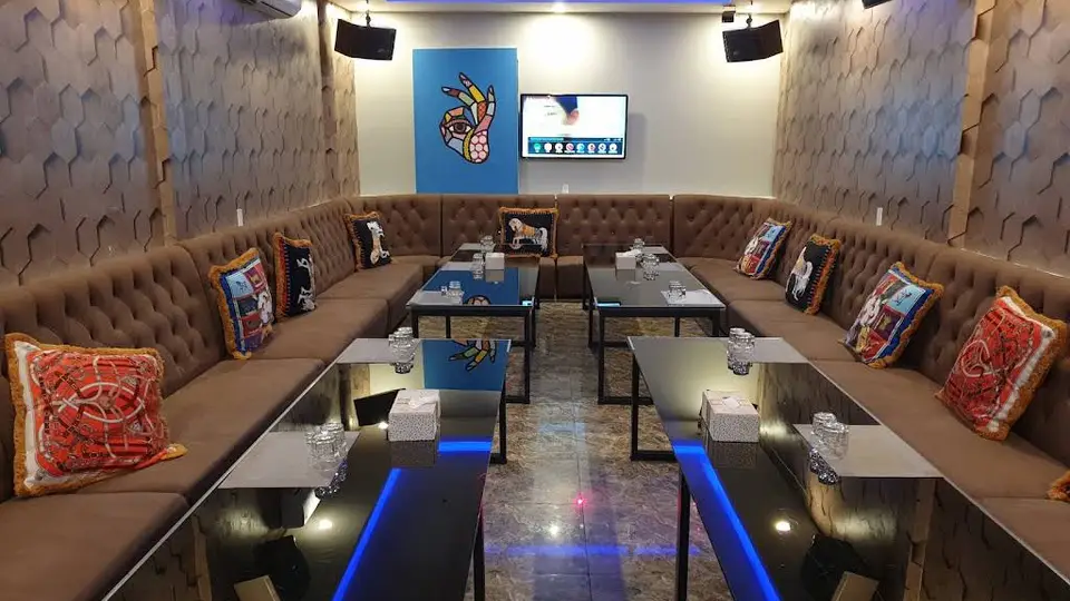 벌집 패턴 벽면과 U자형 갈색 체스터필드 소파, 블루 LED 테이블이 배치된 대형 그룹용 가라오케 룸