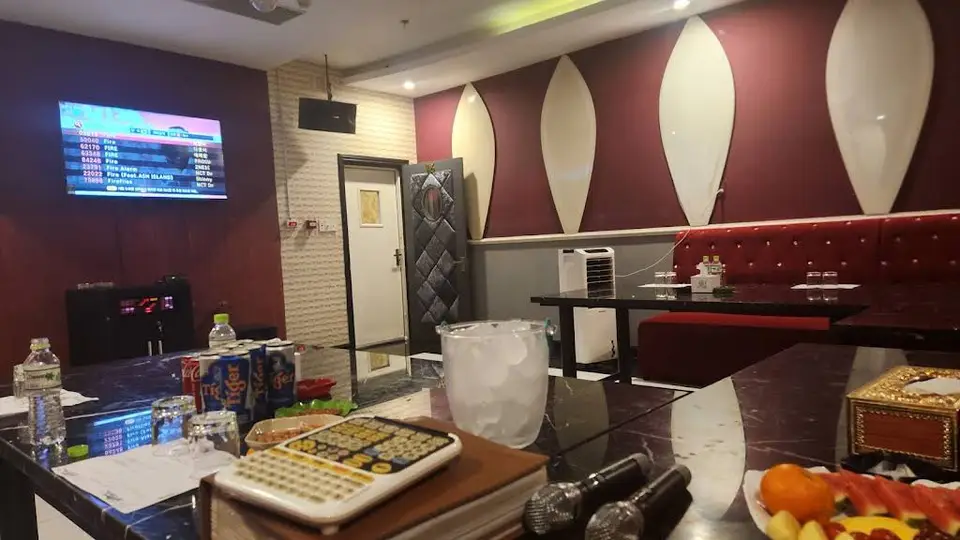 버건디 레드 벽면과 TV 노래방 시스템, 대리석 테이블 위에 음료와 마이크가 준비된 소형 가라오케 룸 내부