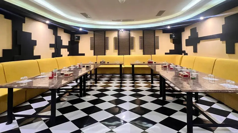 흑백 체크 바닥과 황색 U자형 소파, 대리석 테이블이 배치된 음향 패널로 마감된 대형 가라오케 파티 룸