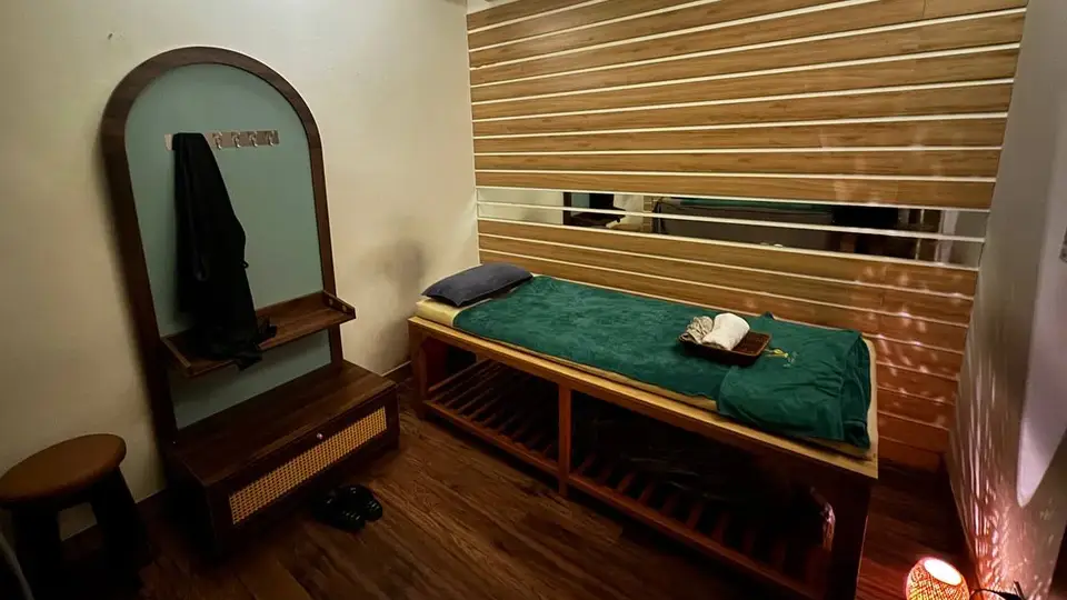 청룡열차 룸 내부의 그린 커버 원목 마사지 베드와 아치형 거울, 우드 슬랫 벽면 인테리어