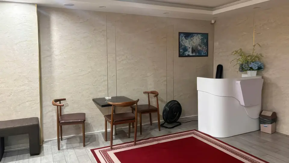 아이보리 대리석 벽면, 레드 카펫, 목재 의자와 화이트 프런트 데스크가 배치된 고급 리셉션 공간