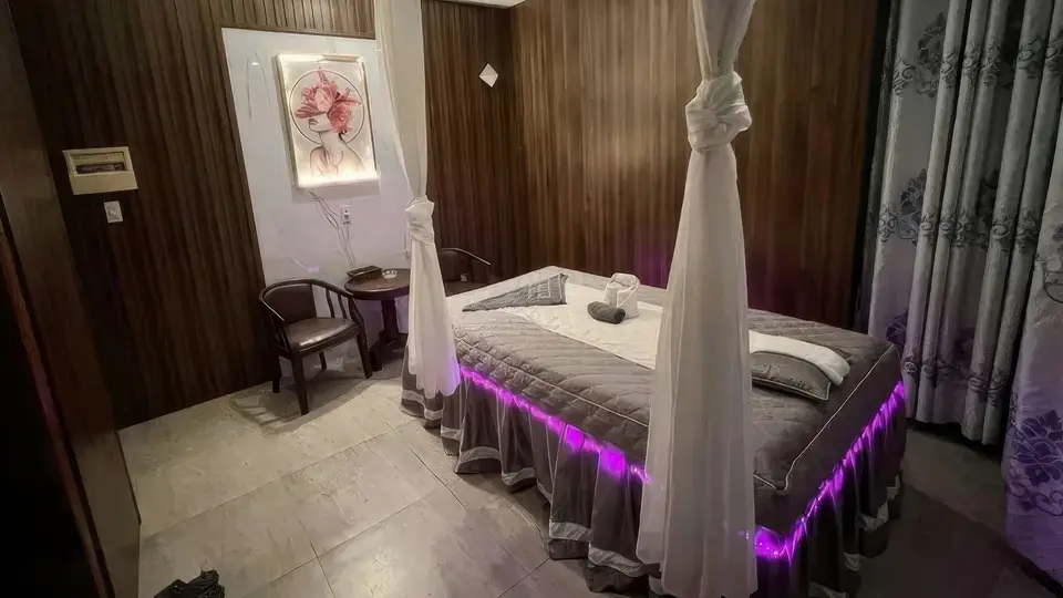 캐노피 침대와 보라색 LED 조명이 어우러진 고급 마사지 룸 내부