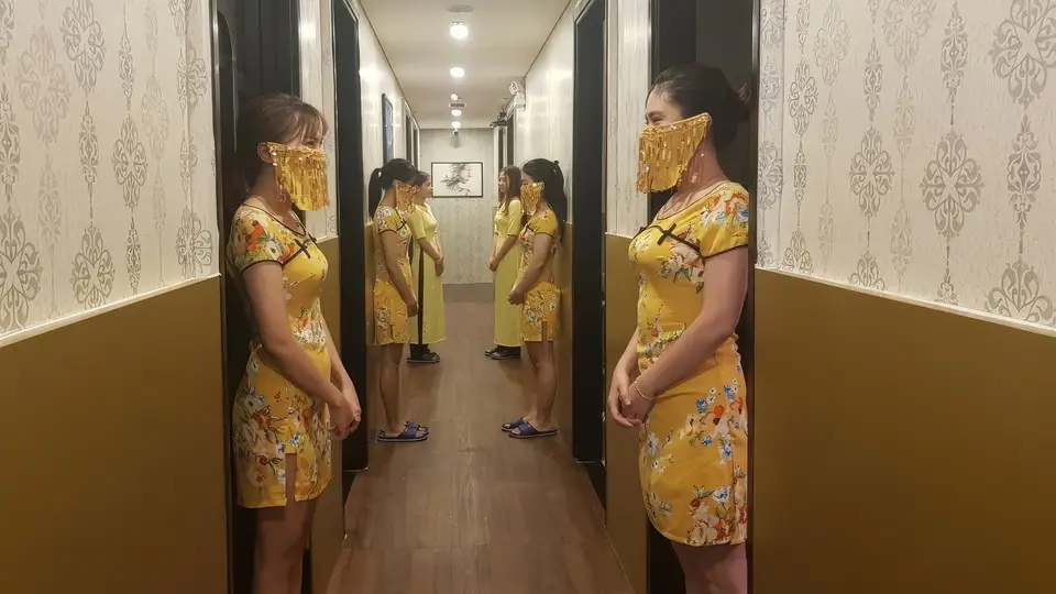 풍투이 마사지의 전통 치파오 유니폼을 착용한 전문 여성 테라피스트 두 명이 복도에 나란히 서 있는 모습