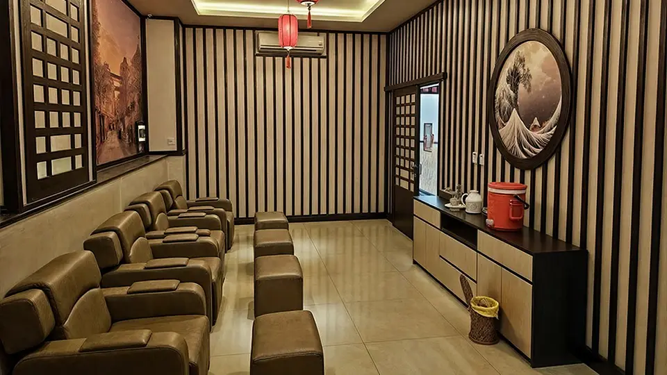 줄지어 배치된 갈색 가죽 리클라이너 의자와 풋 레스트, 붉은 홍등과 일본 수묵화로 장식된 풋 마사지 룸