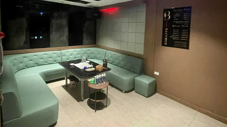 민트 컬러 버튼 터프티드 U형 소파와 다크 그레이 패딩 벽, BACCHUS 메뉴판이 비치된 VIP 룸 내부