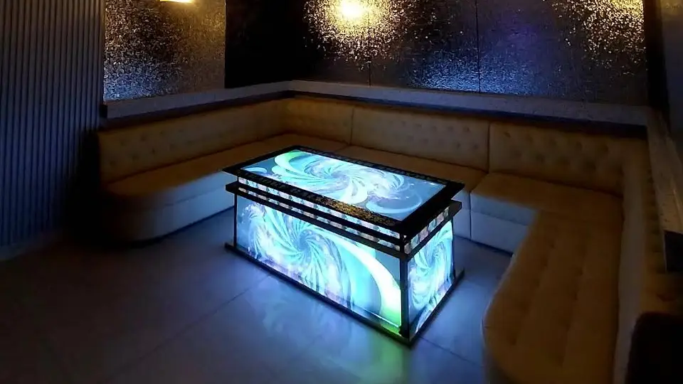 어두운 VIP 라운지 안에서 화이트·민트 컬러의 소용돌이 그래픽으로 빛나는 대형 LED 테이블