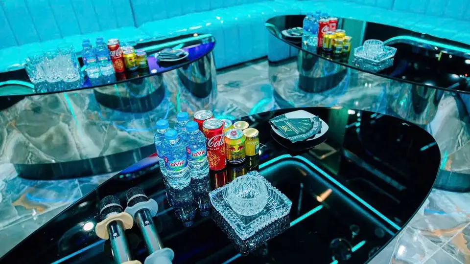 테이블 위에 생수·콜라·레드불·맥주 캔과 크리스탈 재떨이, 마이크가 세팅된 비너스 가라오케의 아쿠아 룸 클로즈업