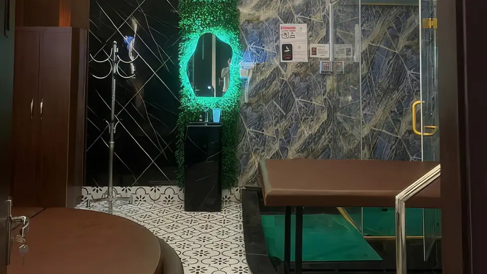 98 스파의 프라이빗 룸 내부, 에메랄드 LED 조명의 식물 장식 거울, 화려한 대리석 패턴 벽면, 풋 스파 베드 및 유리 샤워 부스