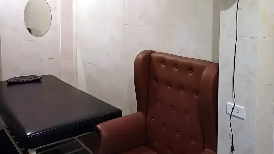 어메이징 마사지 룸 내부의 고급 갈색 윙체어와 블랙 마사지 베드, 원형 거울이 배치된 프라이빗 룸