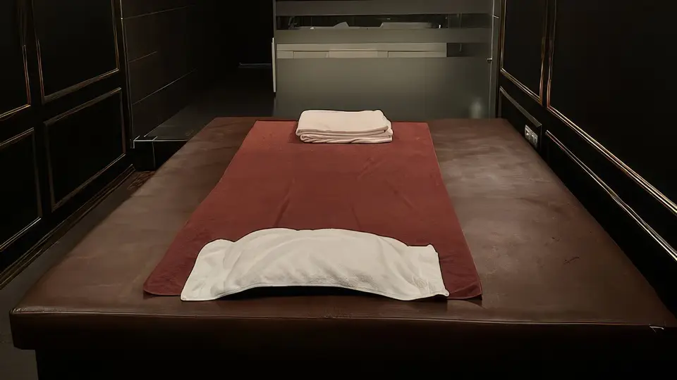 블랙 골드 패널 벽면과 정갈하게 세팅된 마사지 베드, 청결한 타월이 준비된 고급 마사지 룸 내부
