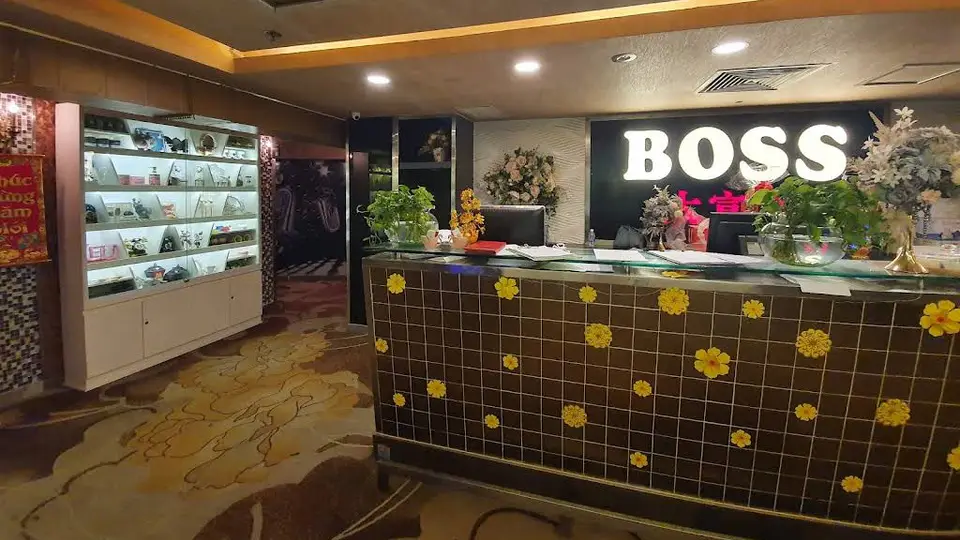BOSS 로고 조명과 꽃 장식 타일 카운터, 진열장이 배치된 보스 가라오케의 메인 리셉션 전경