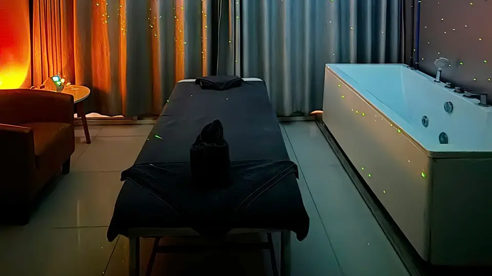 어두운 조명 속 블랙 마사지 베드와 LED 조명이 감싸진 대형 자쿠지 욕조가 배치된 스파 룸