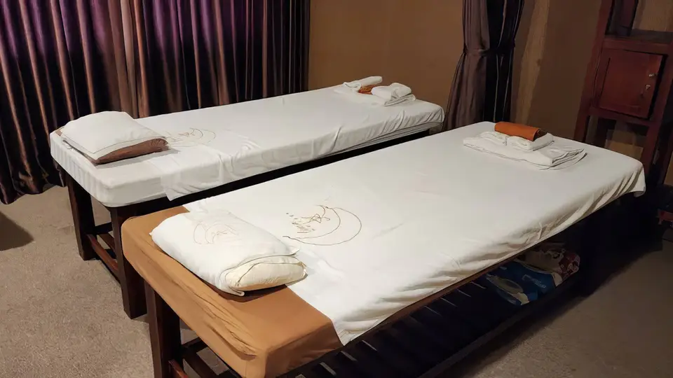 루나 마사지 로고가 수놓인 흰 시트의 마사지 베드 두 개가 나란히 놓인 커플 전용 마사지 룸