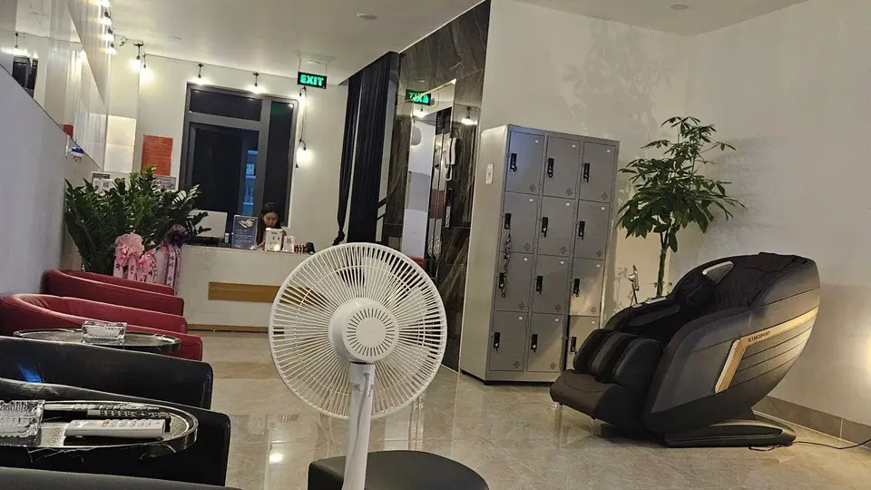 슈퍼맨 마사지 로비 전경 — 붉은 소파와 검정 안락의자, 무인 사물함, 고급 전자동 마사지 체어, 리셉션 직원이 배치된 밝고 넓은 대기 공간