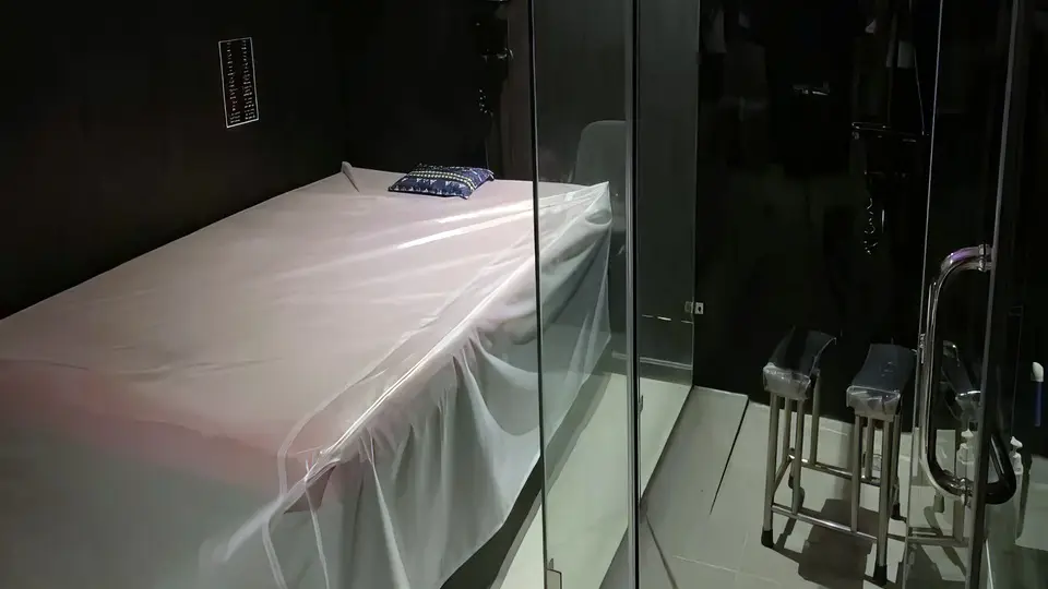 슈퍼맨 마사지 룸 내부 — 흰색 시트로 정갈하게 정돈된 마사지 베드, 유리 파티션 너머 샤워 공간과 발 받침대가 완비된 독립 룸