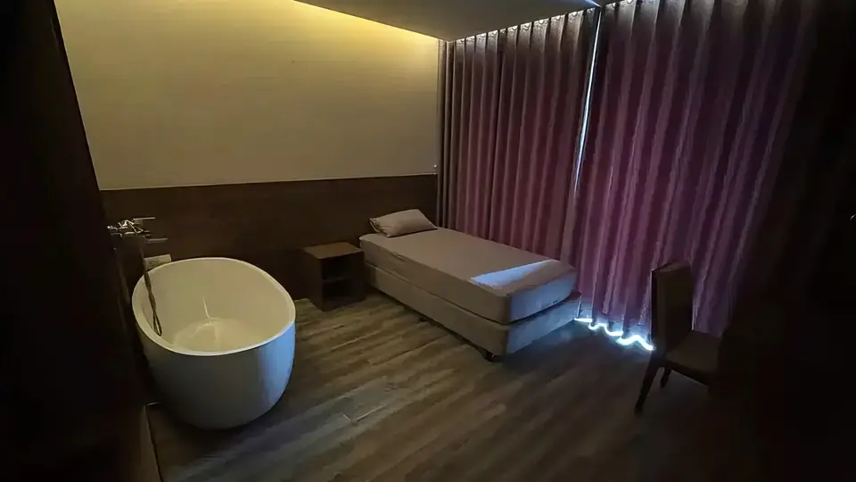 어두운 조명과 보라빛 커튼이 드리워진 프라이빗 스파 룸, 대형 원형 독립 욕조와 싱글 마사지 베드