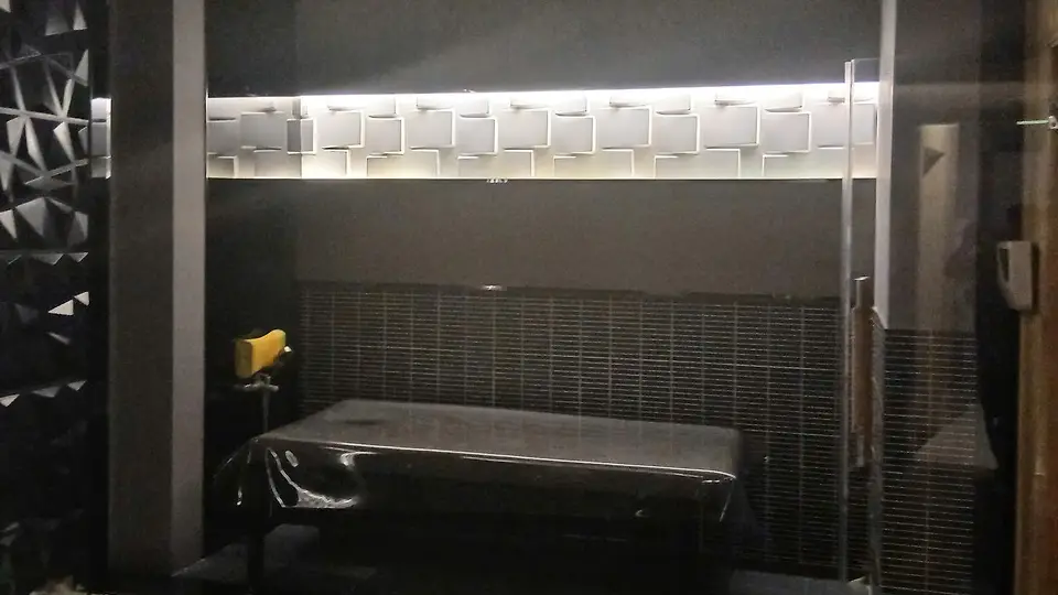 화이트 큐브 패턴 조명 월과 유리 파티션, 블랙 마사지 베드가 조화를 이루는 다크 톤 테라피 룸