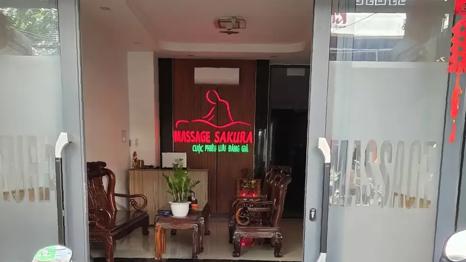 사쿠라 마사지 입구 전경, 붉은 네온 조명과 전통 목재 의자가 배치된 웰컴 공간