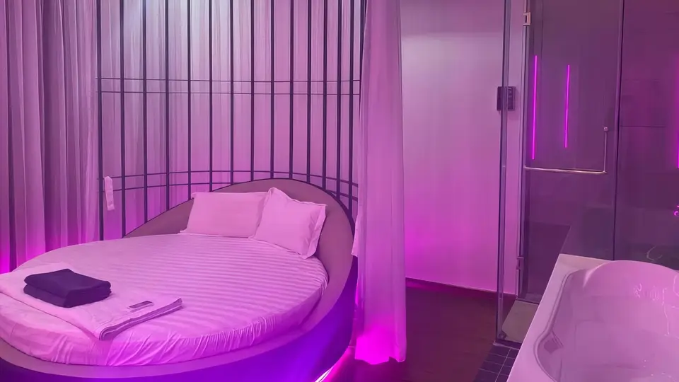보랏빛 무드 조명 아래 대형 원형 침대와 유리 샤워 부스, 자쿠지 욕조가 배치된 VIP 스위트 룸